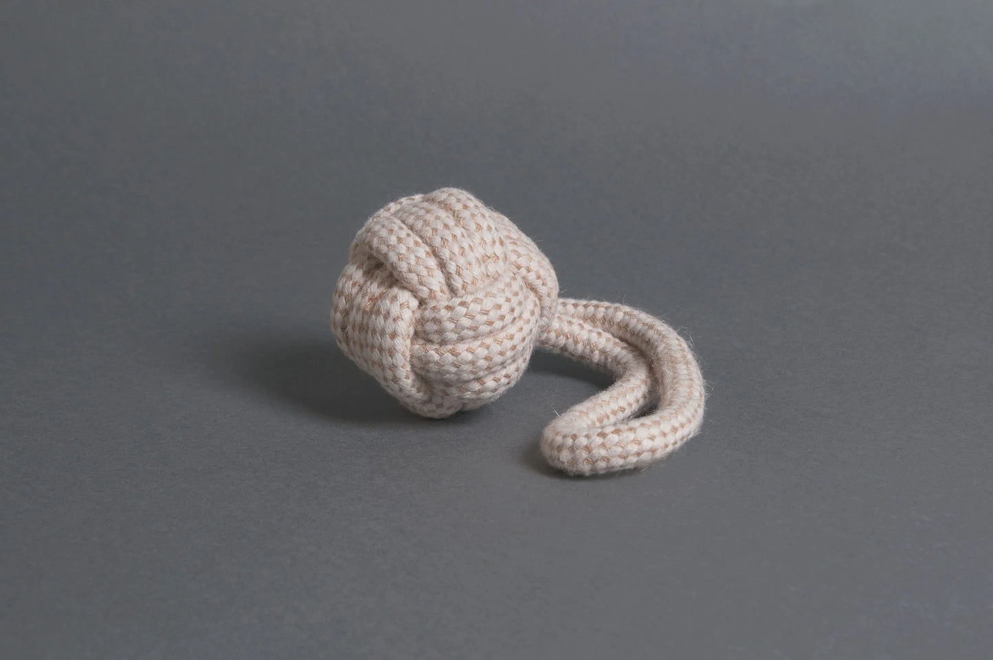 The Hilltop Pet Food Natural Rope Toy - Slingshot Ball is tied in a monkey’s fist knot with a loose end on gray.