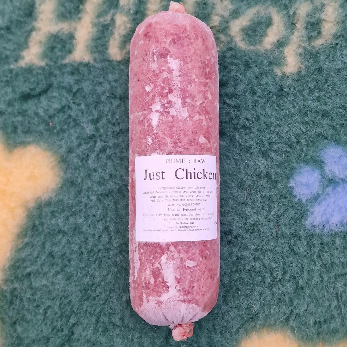 A roll of Hilltop Pet Food Prime:Raw - Just Chicken, a complementary feed, on a green and yellow paw print blanket.