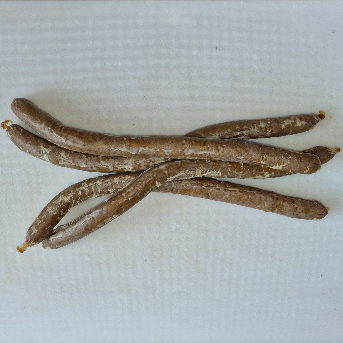 Three sausages on a white cutting board.