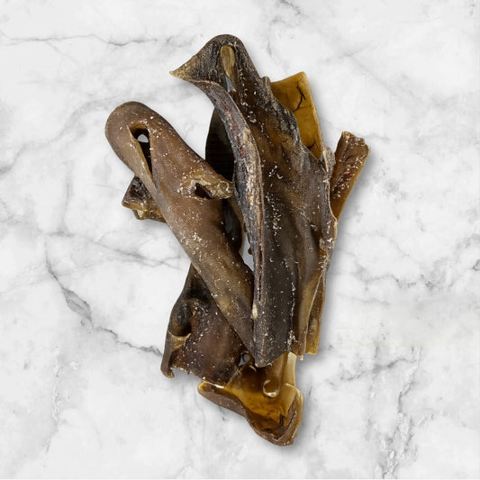 Three Hilltop Pet Food Camel Skin dog chews are stacked on a white marble surface.