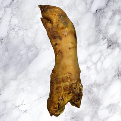 A Hilltop Pet Food Large Pig Trotter—dried and natural—rests on a white marble surface.