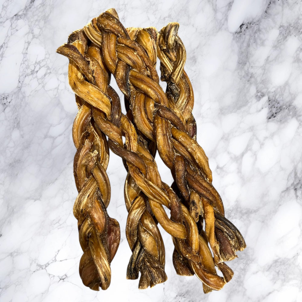 Three Hilltop Pet Food Braided Pizzle Bully Stick treats are arranged side by side on a marble surface.