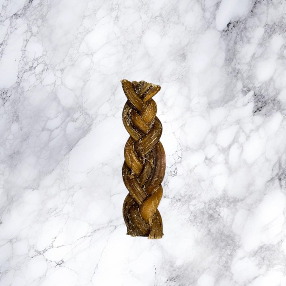 A single Hilltop Pet Food Braided Pizzle Bully Stick rests on white marble, perfect as a natural dog treat.