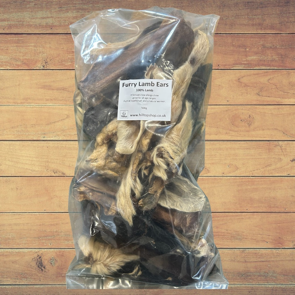 A clear bag of Hilltop Pet Food Furry Lamb Ears dog treats rests on wood, label visible.