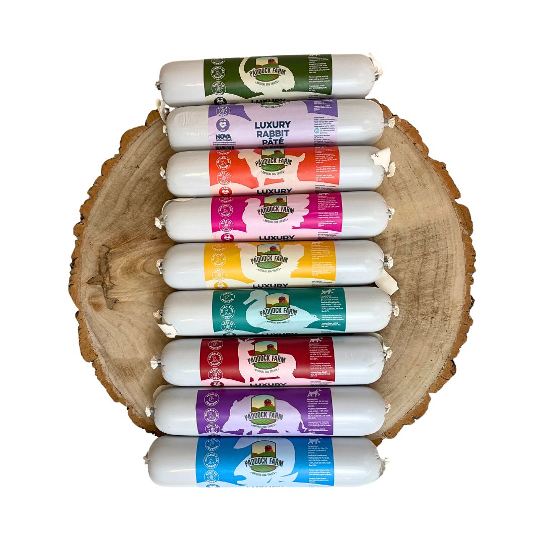 Eight Paddock Farm Luxury Pâté tubes by Hilltop Pet Food, each a different flavor, are lined up on a wooden slab.
