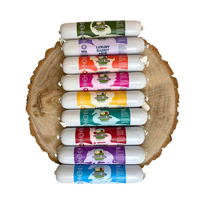 Eight Paddock Farm Luxury Pâté tubes by Hilltop Pet Food, each a different flavor, are lined up on a wooden slab.